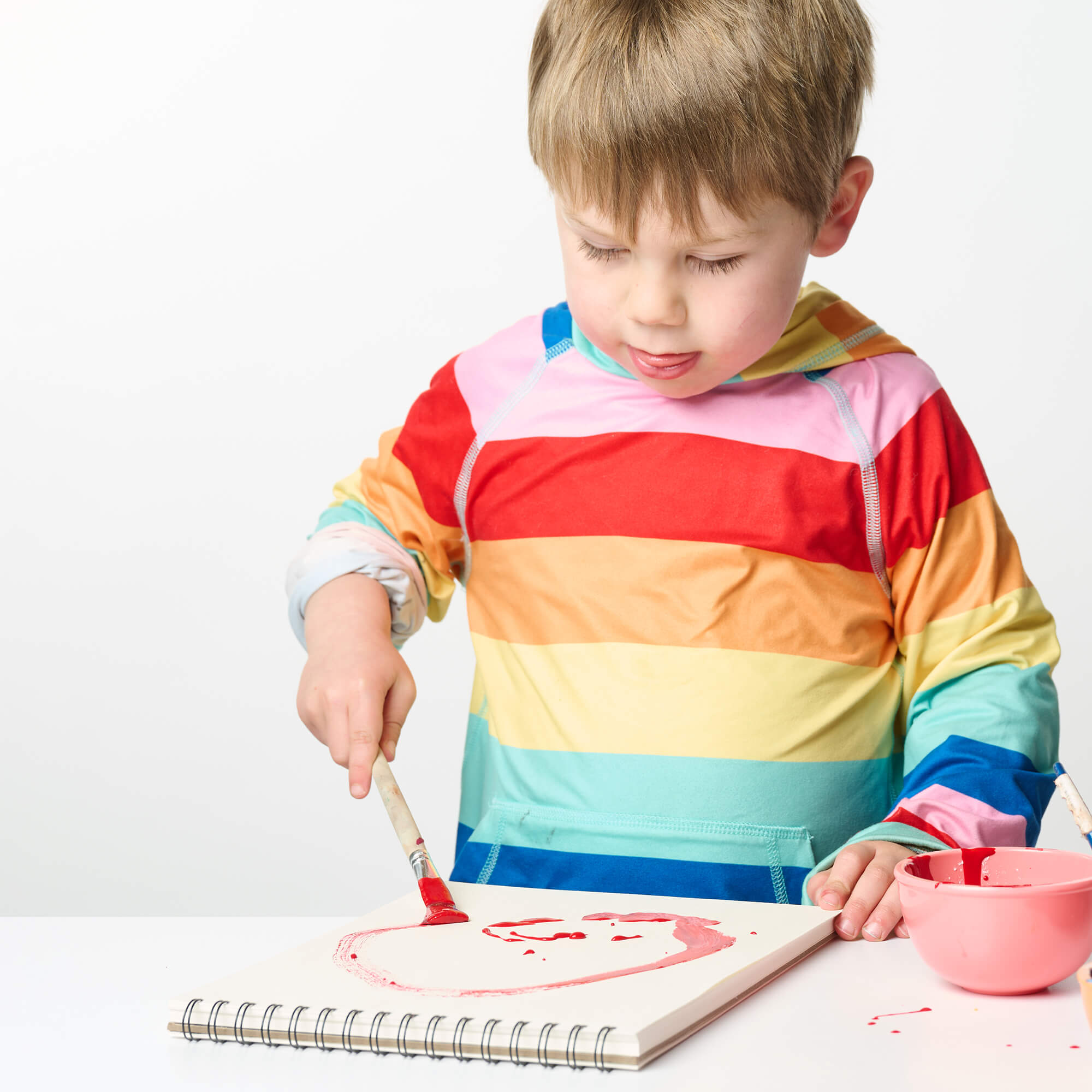 Child in a colorful striped shirt painting on a white surface