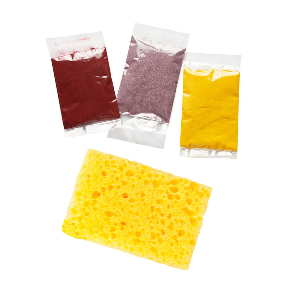 Three packets of colored sand and a yellow sponge on a white background