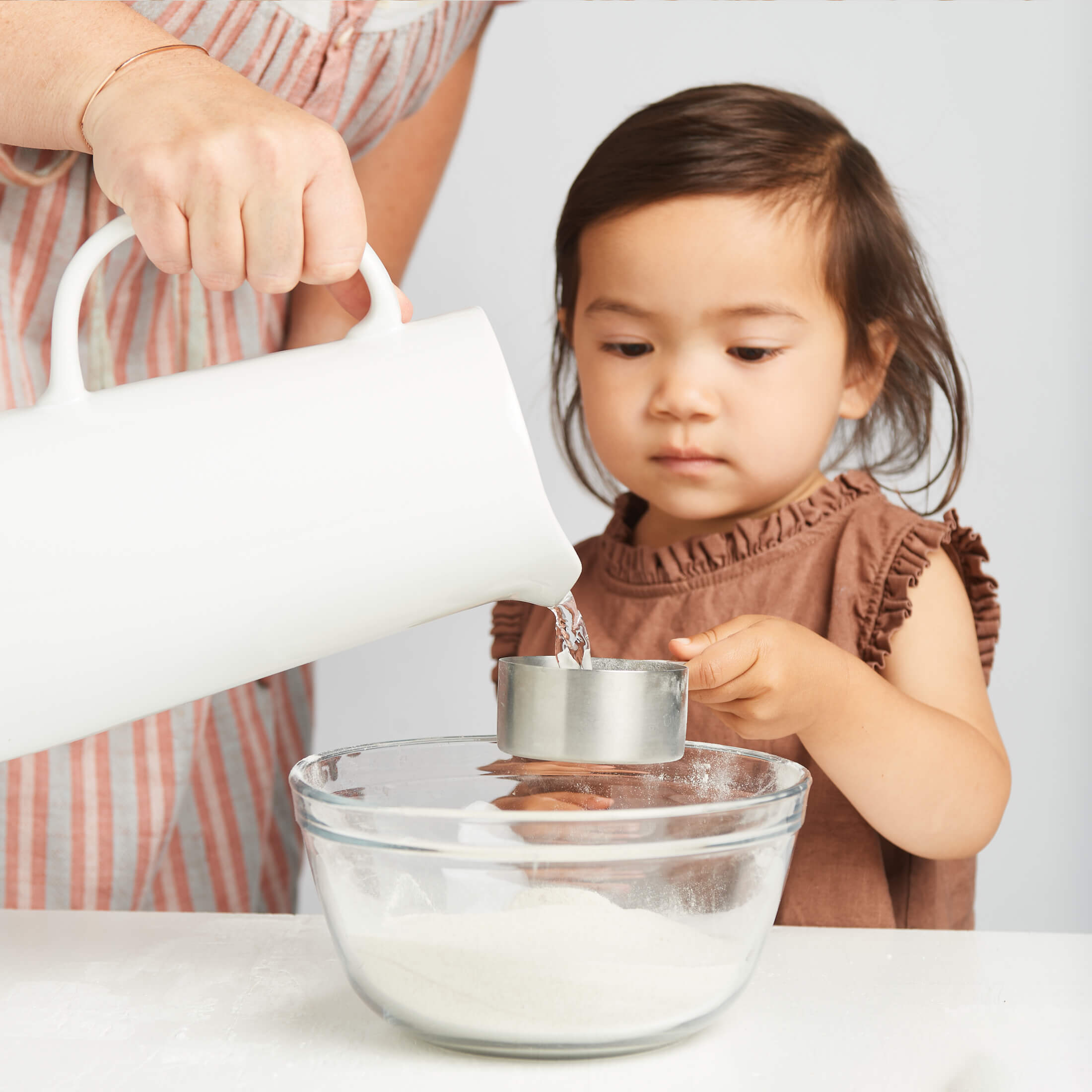 Child helping with a cooking activity by pouring liquid into a bowl