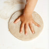 Hand pressing into a round piece of dough on a light background