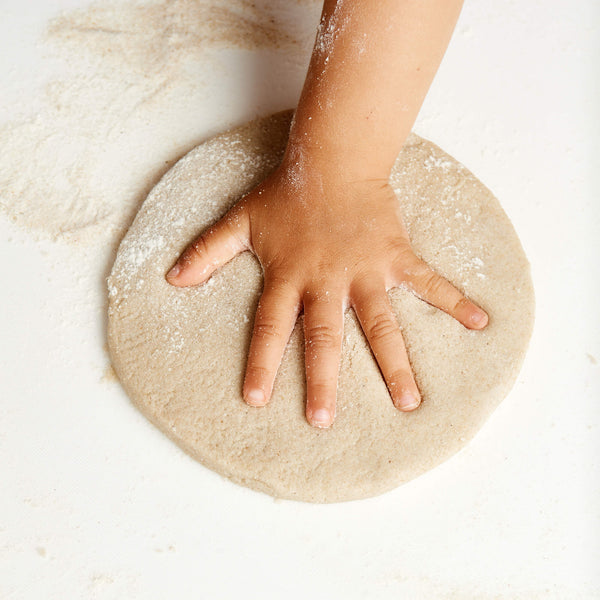 Hand pressing into a round piece of dough on a light background