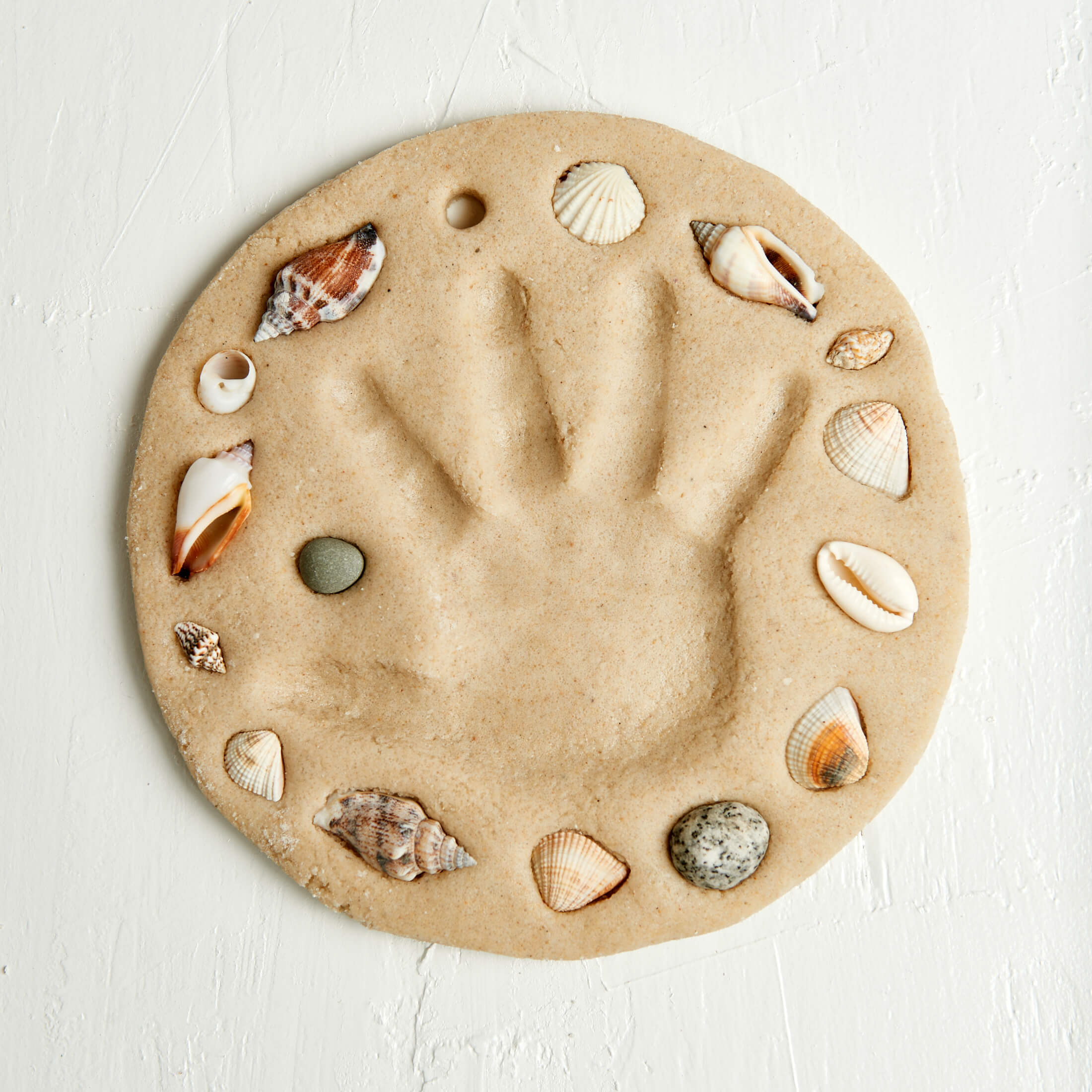 Round sand mold with a handprint and seashells on a white background
