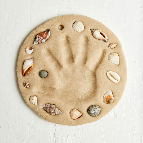 Round sand mold with a handprint and seashells on a white background