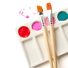 Two paintbrushes on a white palette with red, pink, and blue paint swatches.