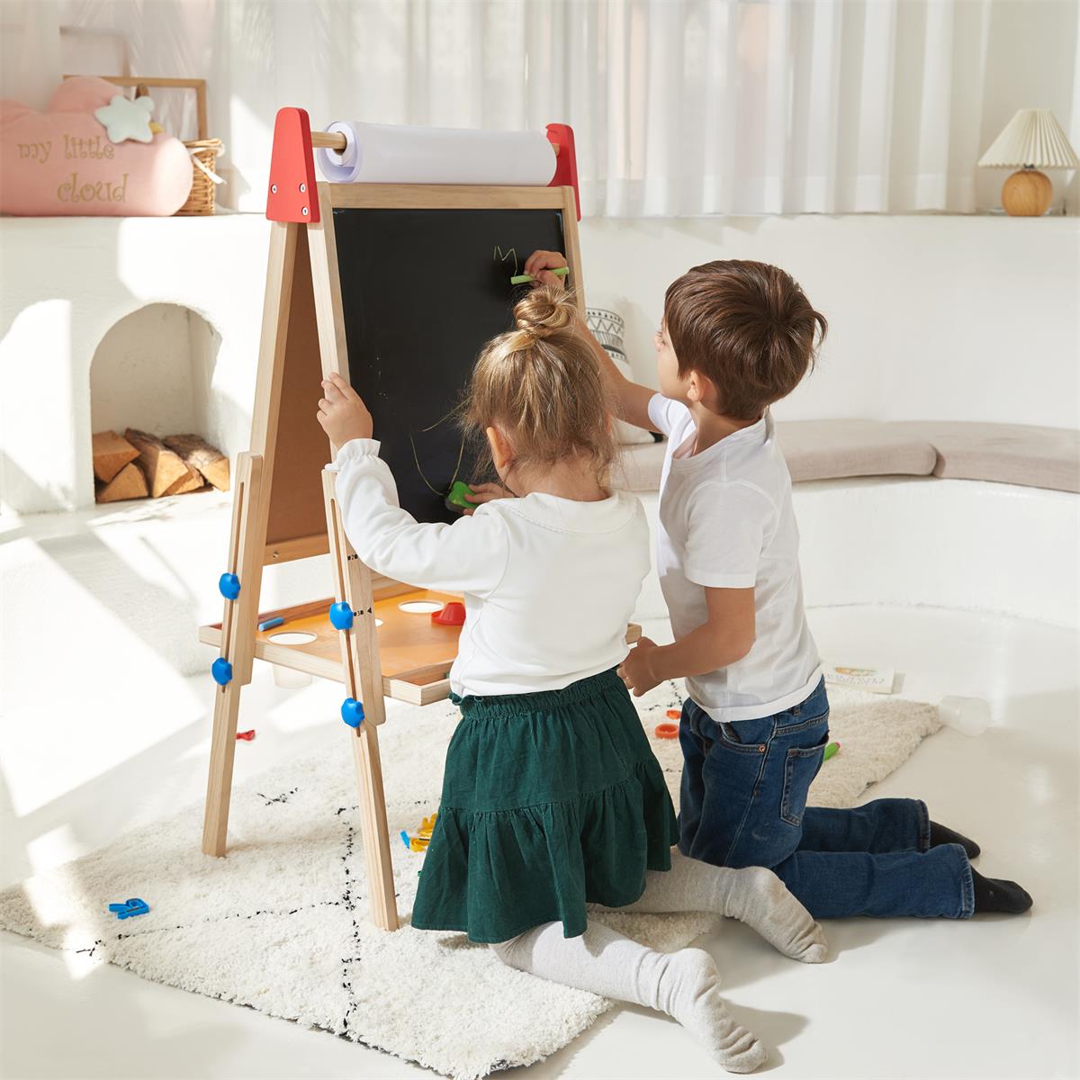 Two children drawing on a blackboard easel in a bright living room.