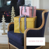 Two gift boxes tied with ribbons on a navy chair in a cozy room with a fireplace.