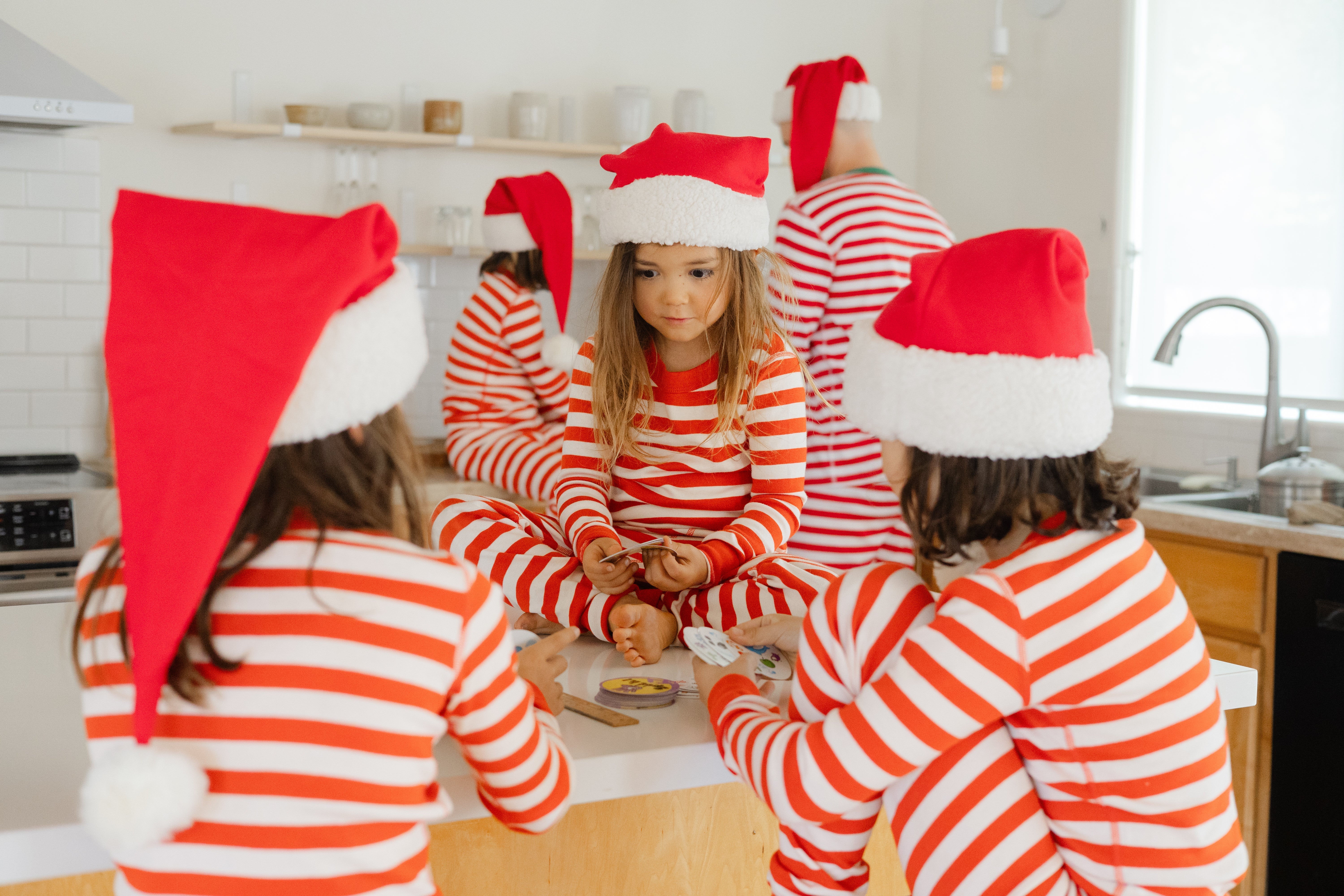 Children wearing red and white striped pajamas and Santa hats in a kitchen.