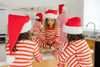 Children wearing red and white striped pajamas and Santa hats in a kitchen.
