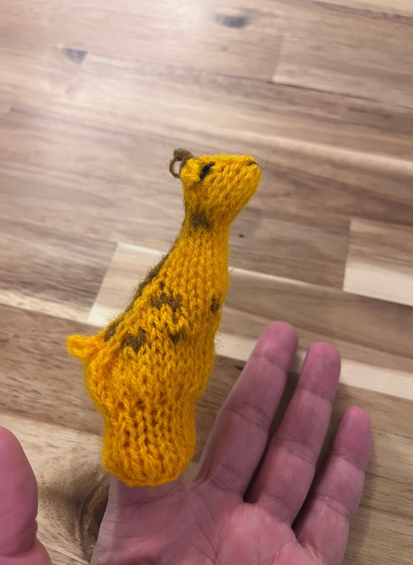 Yellow knitted giraffe puppet finger toy held by a hand on a wooden floor