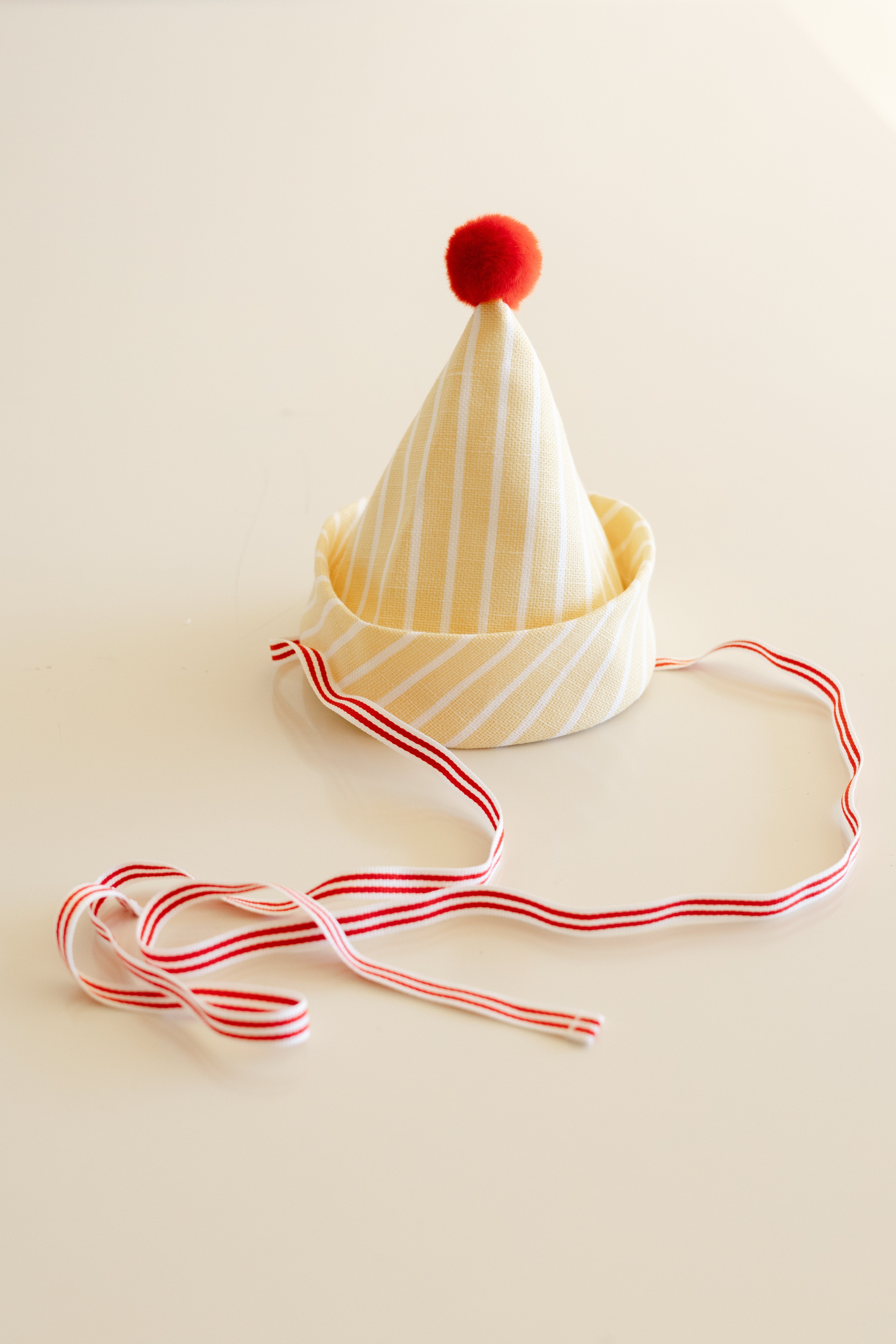 White party hat with red pom-pom and striped ribbon on a beige background