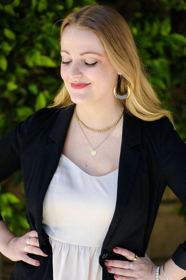 Close-up of Fair Anita hammered crescent loop earrings showing black and brass texture detail