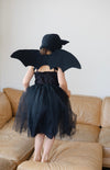 Person wearing a black dress with bat wings standing on a beige couch.