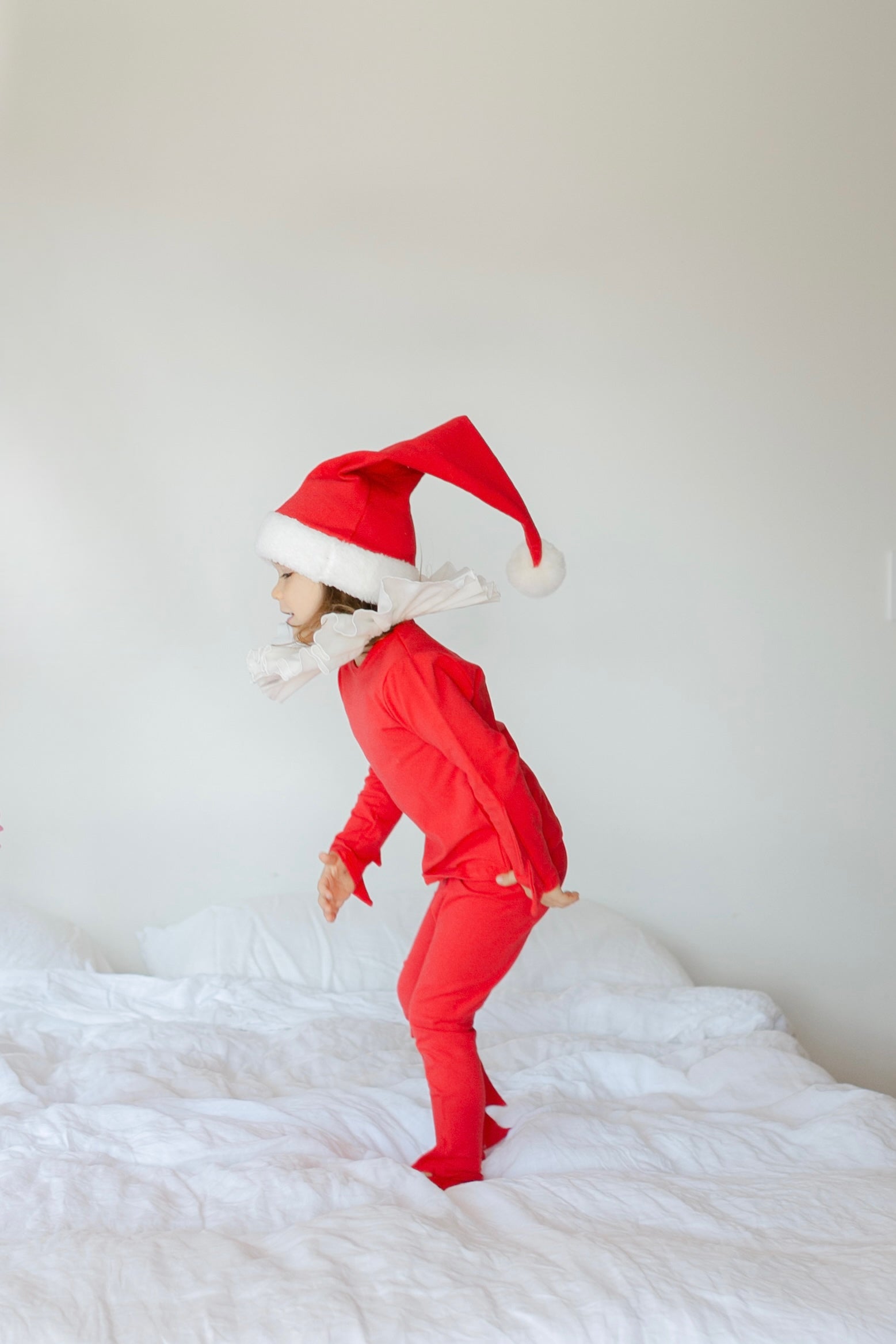 Person wearing a red Santa hat and matching outfit on a white bed.