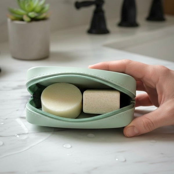 Hand holding a mint green case with two bars of soap on a bathroom counter.