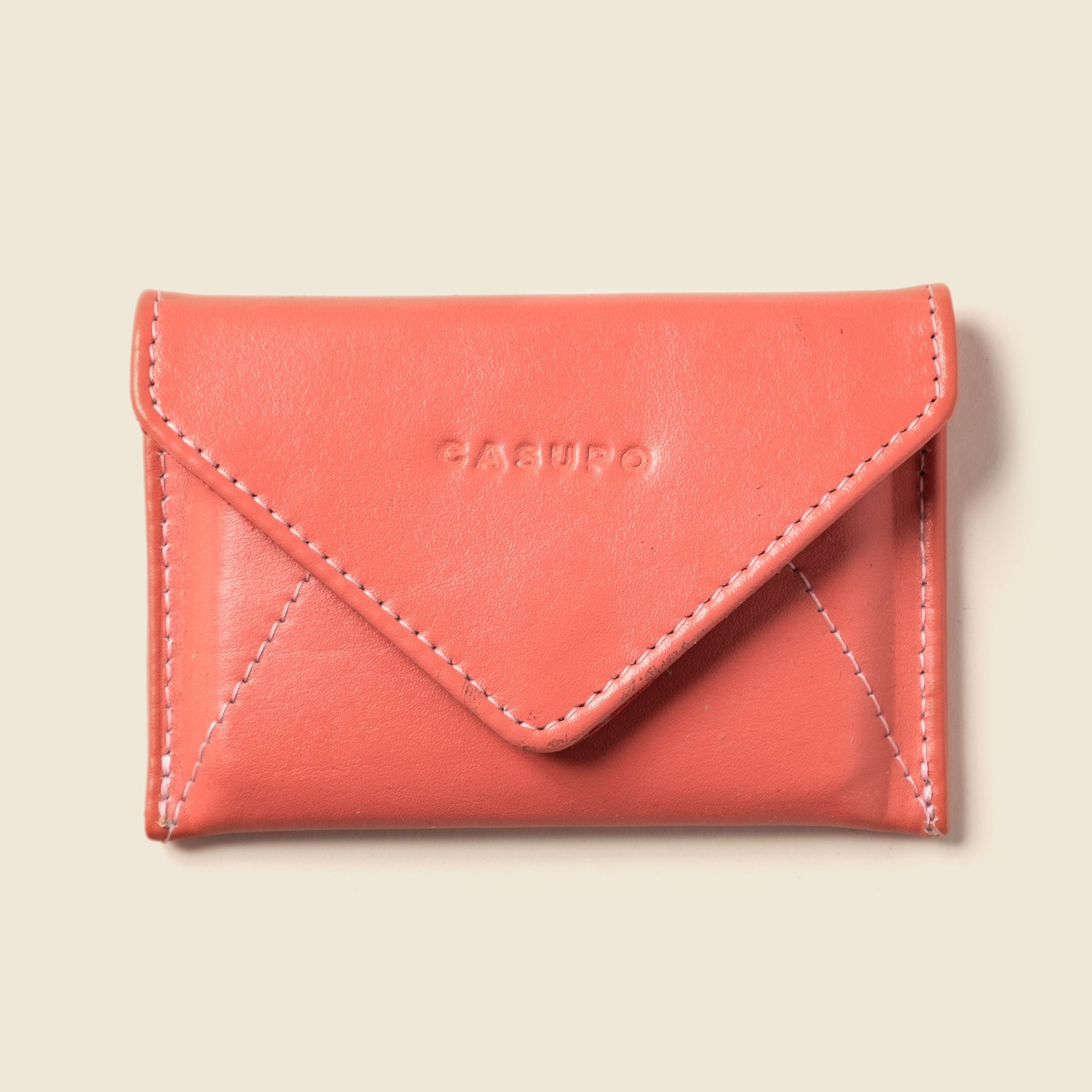 Coral-colored wallet with 'Casu' branding on a beige background