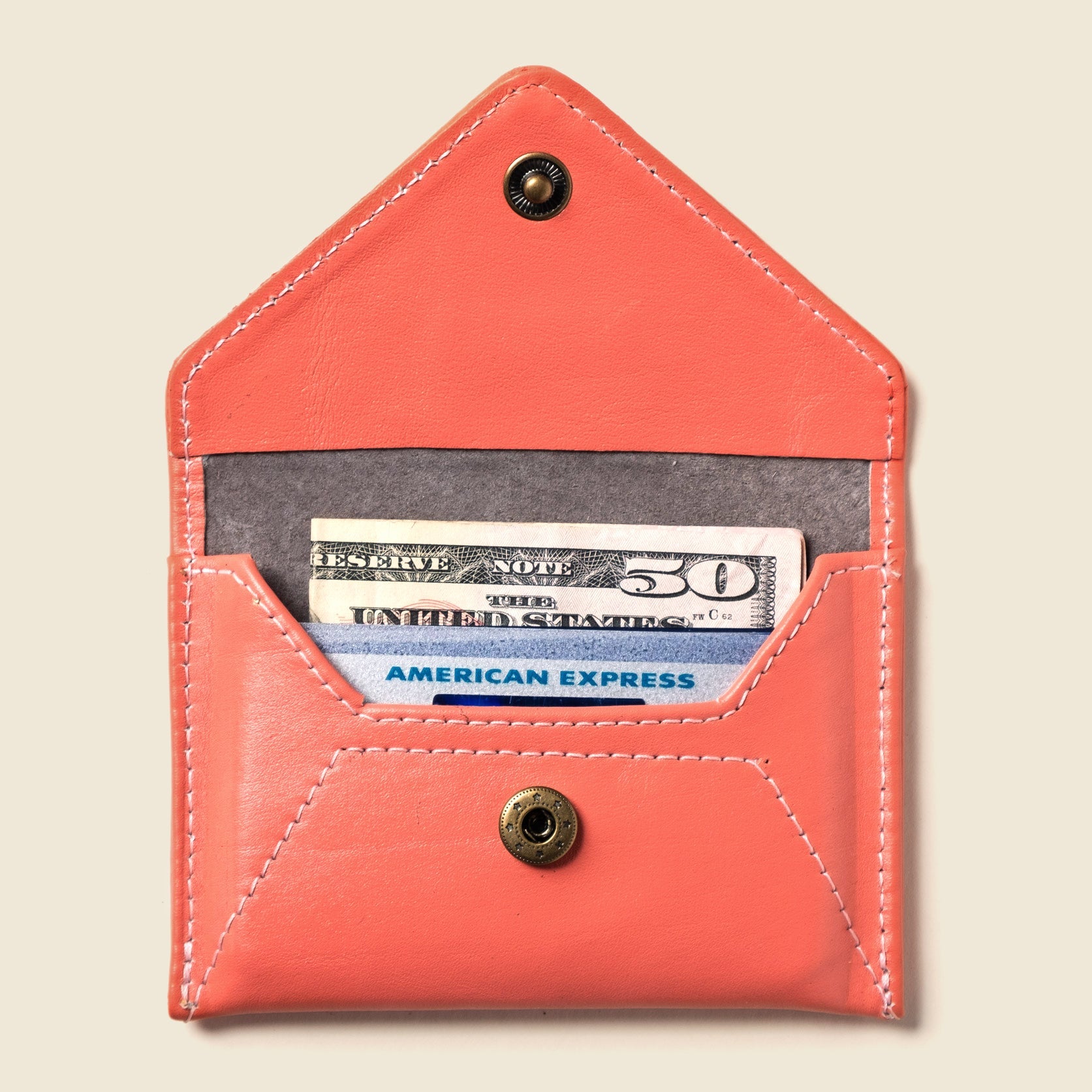Coral leather wallet with American Express card and cash on a beige background