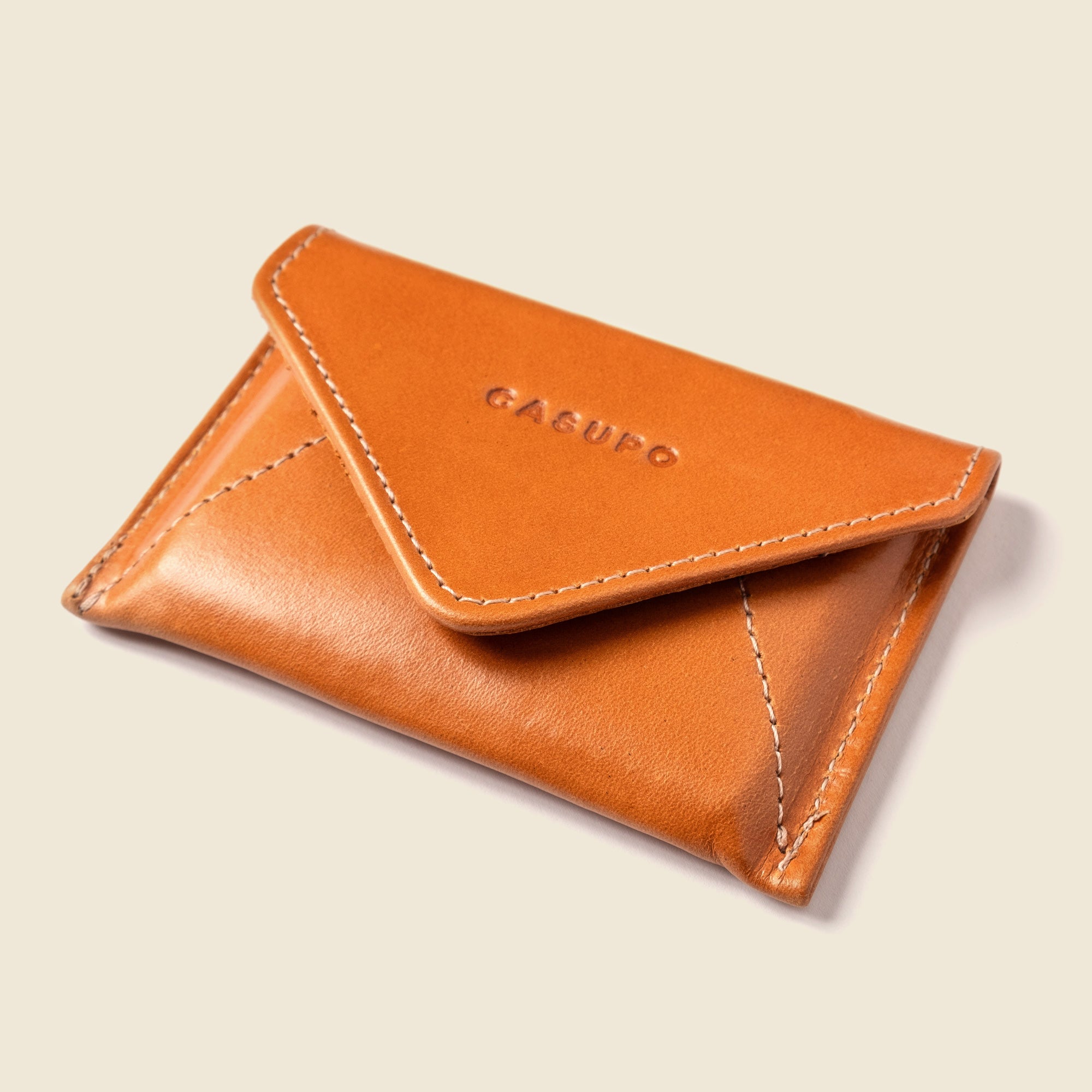 Brown leather cardholder with 'Casu' branding on a beige background