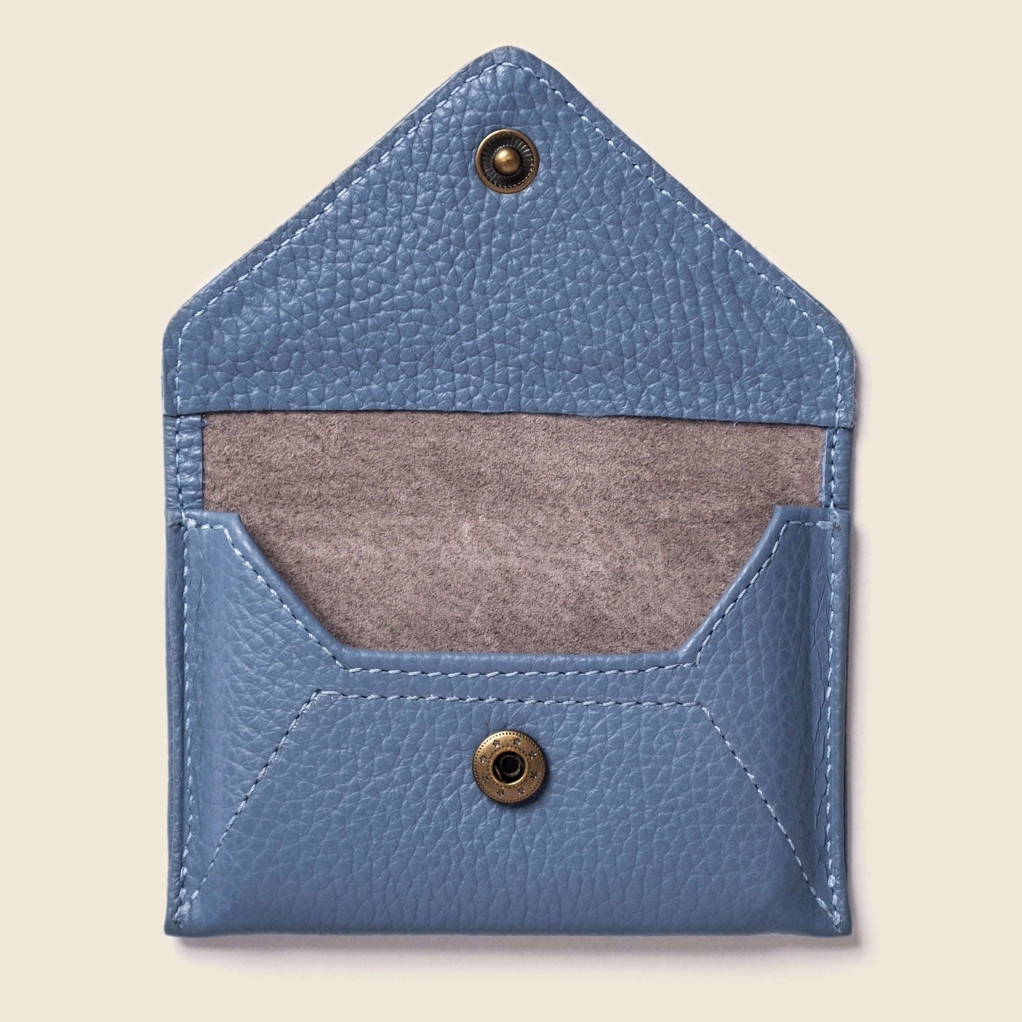 Blue leather cardholder with brass buttons on a beige background