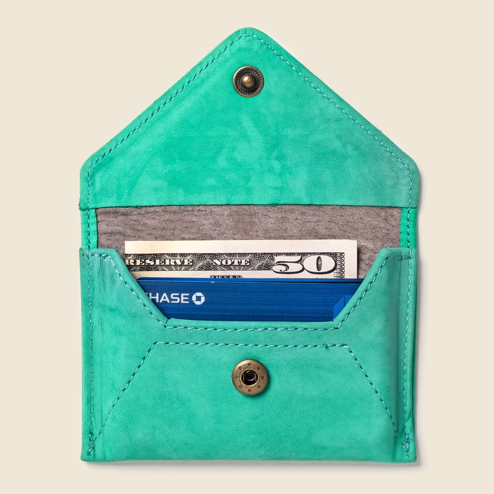 Turquoise cardholder with money and a card inside on a beige background