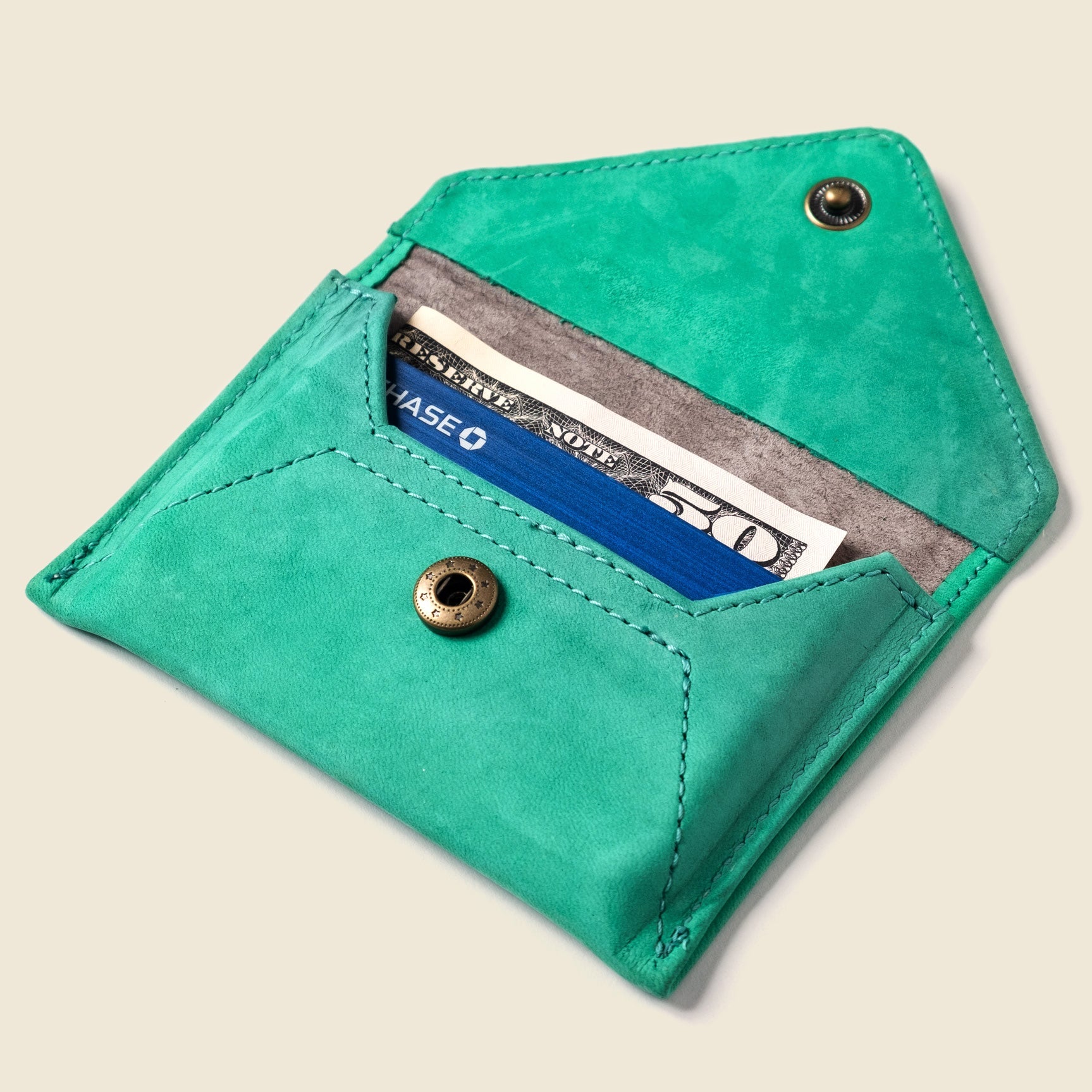 Turquoise leather wallet with a card inside on a beige background