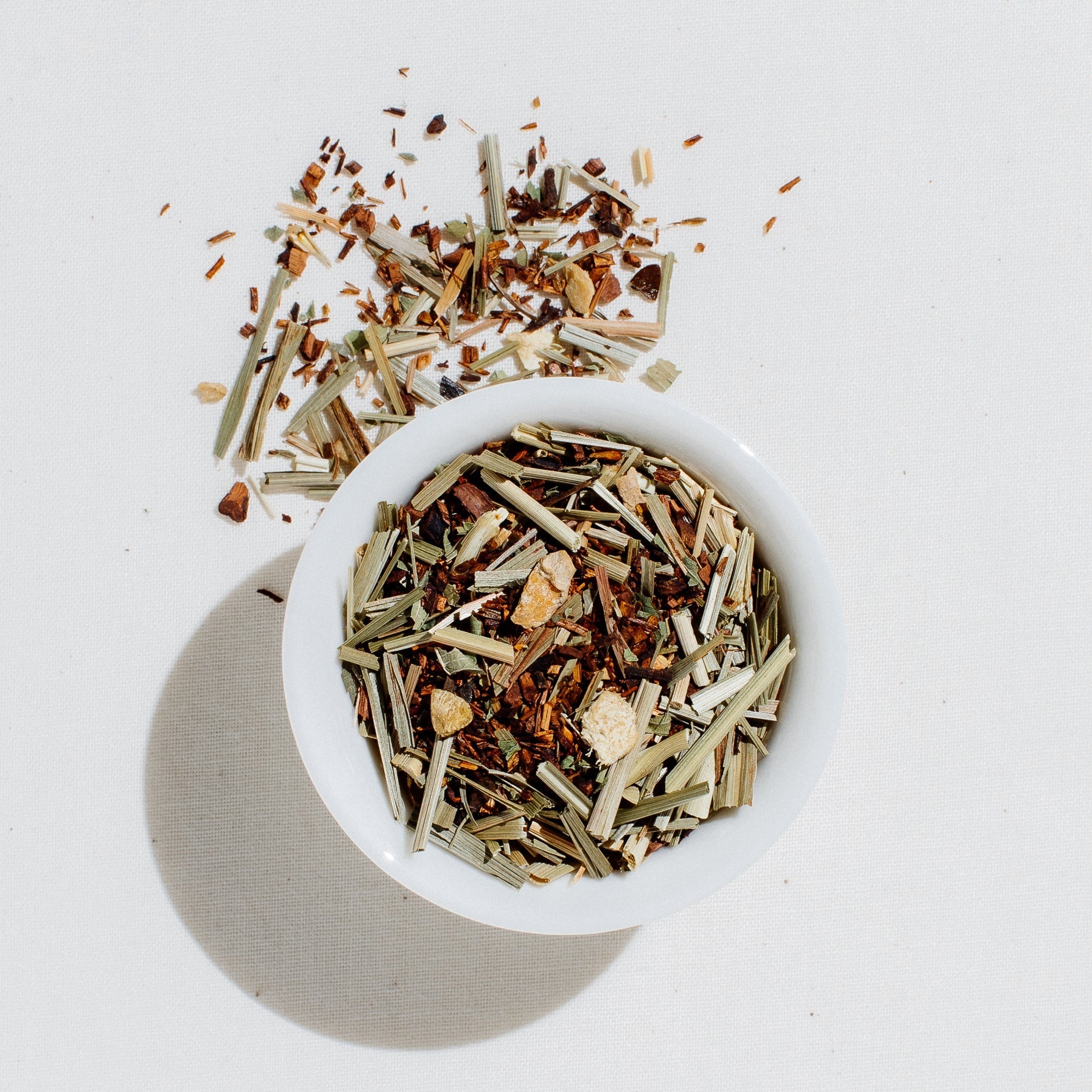 Loose leaf French Lemon Ginger organic herbal tea blend with dried ginger, lemongrass, and lemon verbena in a white bowl on a light gray background
