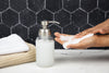 Hand soap dispenser with soapy hands against a black tiled wall.