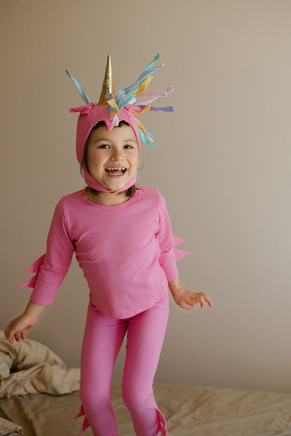 Child wearing a pink unicorn costume with a colorful horn on a plain background