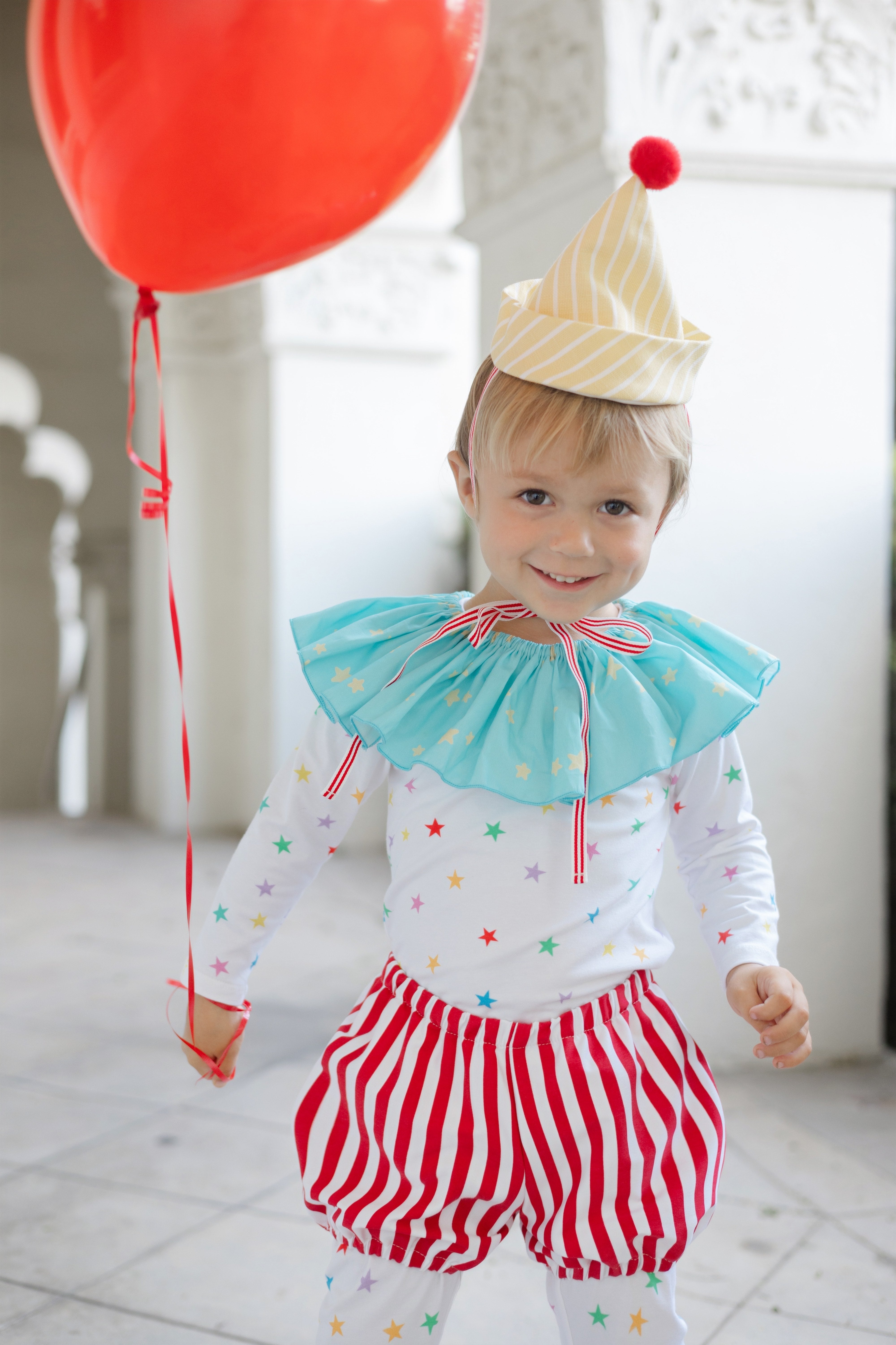 Child in clown costume with red balloon indoors