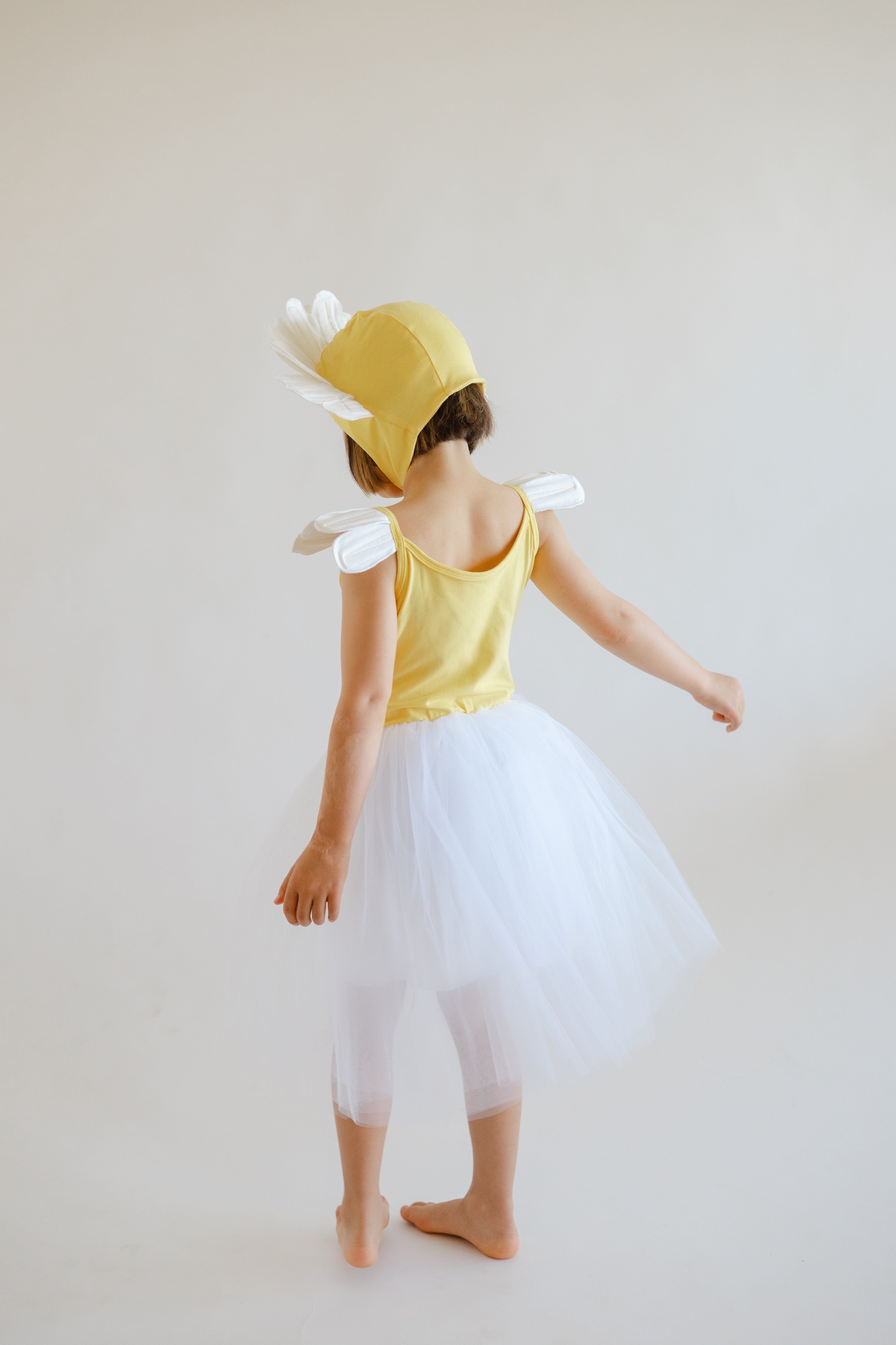 Child wearing a yellow dress with white wings and a yellow hat on a plain background