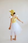 Child wearing a yellow dress with white wings and a yellow hat on a plain background