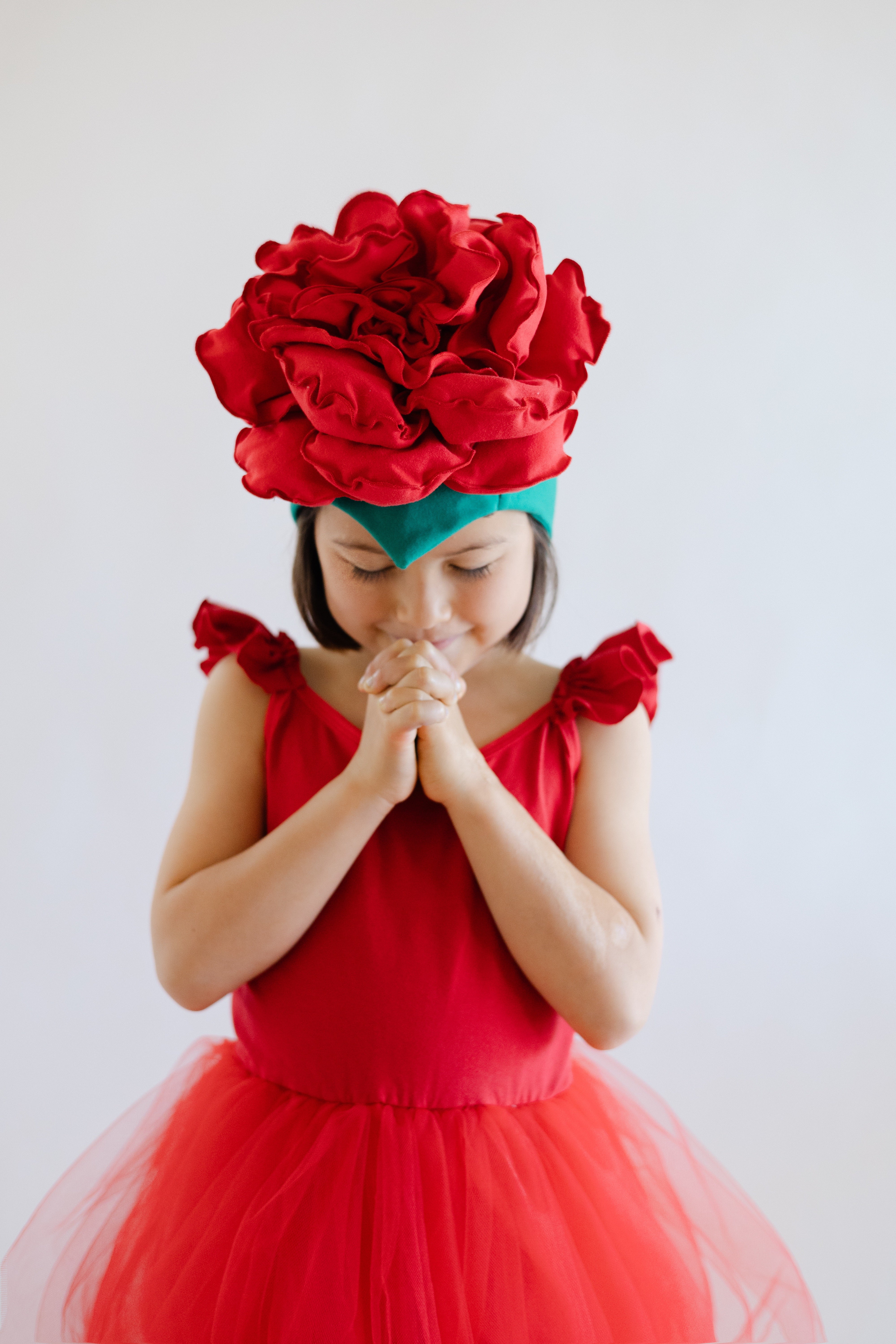 Young girl in a red dress with a large red flower headpiece on a white background
