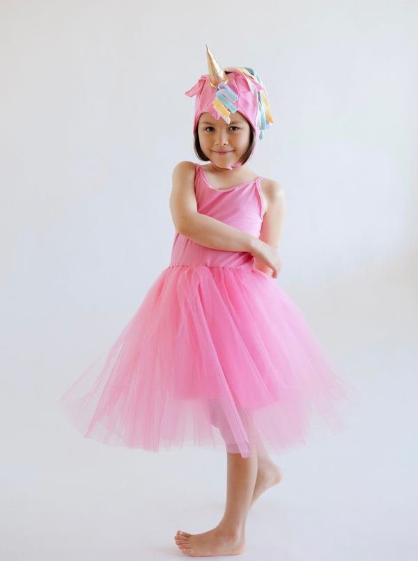 Child wearing a pink dress and unicorn hat on a white background
