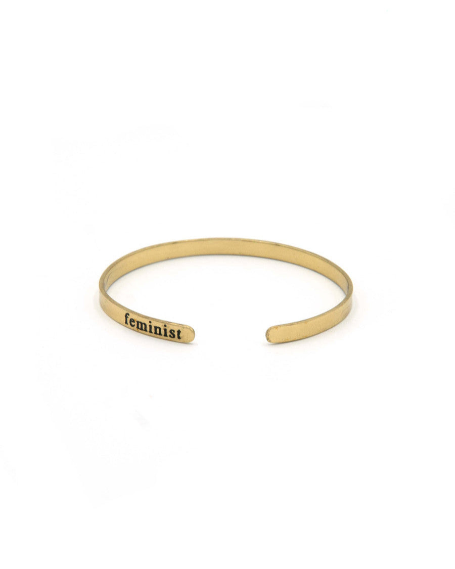 Gold bracelet with 'feminist' engraving on a white background