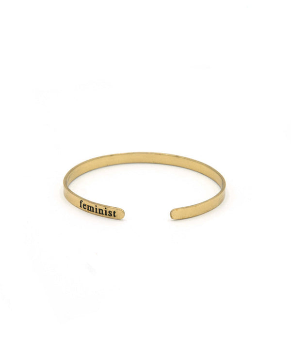 Gold bracelet with 'feminist' engraving on a white background