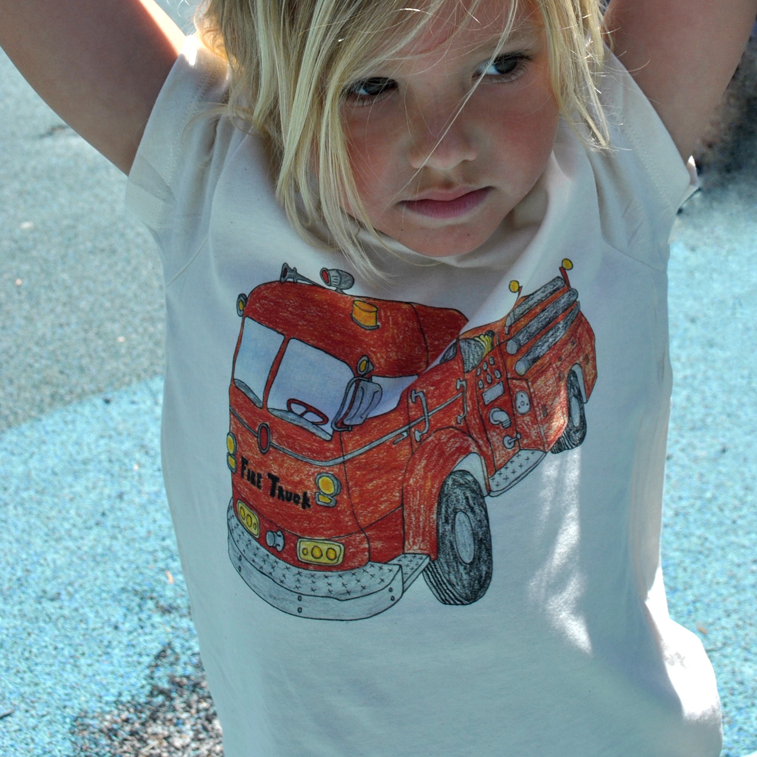 Child wearing a white t-shirt with a red fire truck graphic on a sandy background