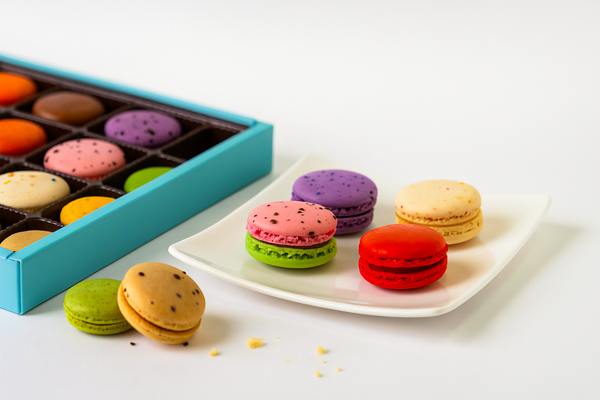 Colorful macarons on a white plate with a box of assorted chocolates in the background.