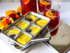 Fruit ice cube tray with fruits and glasses of juice on a white surface