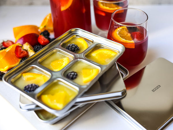 Fruit ice cube tray with fruits and glasses of juice on a white surface