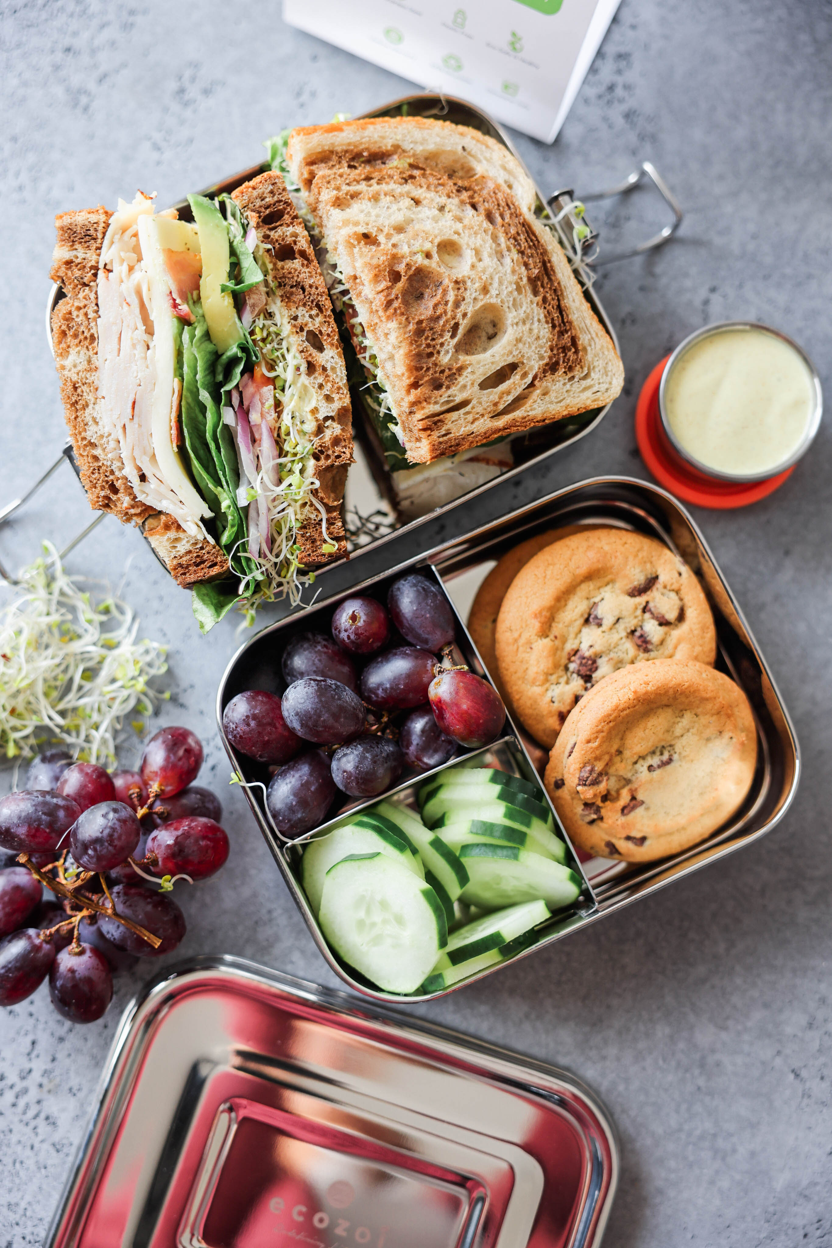 Ecozoi plastic-free stainless steel lunch box with mini sauce container and orange band on wooden surface