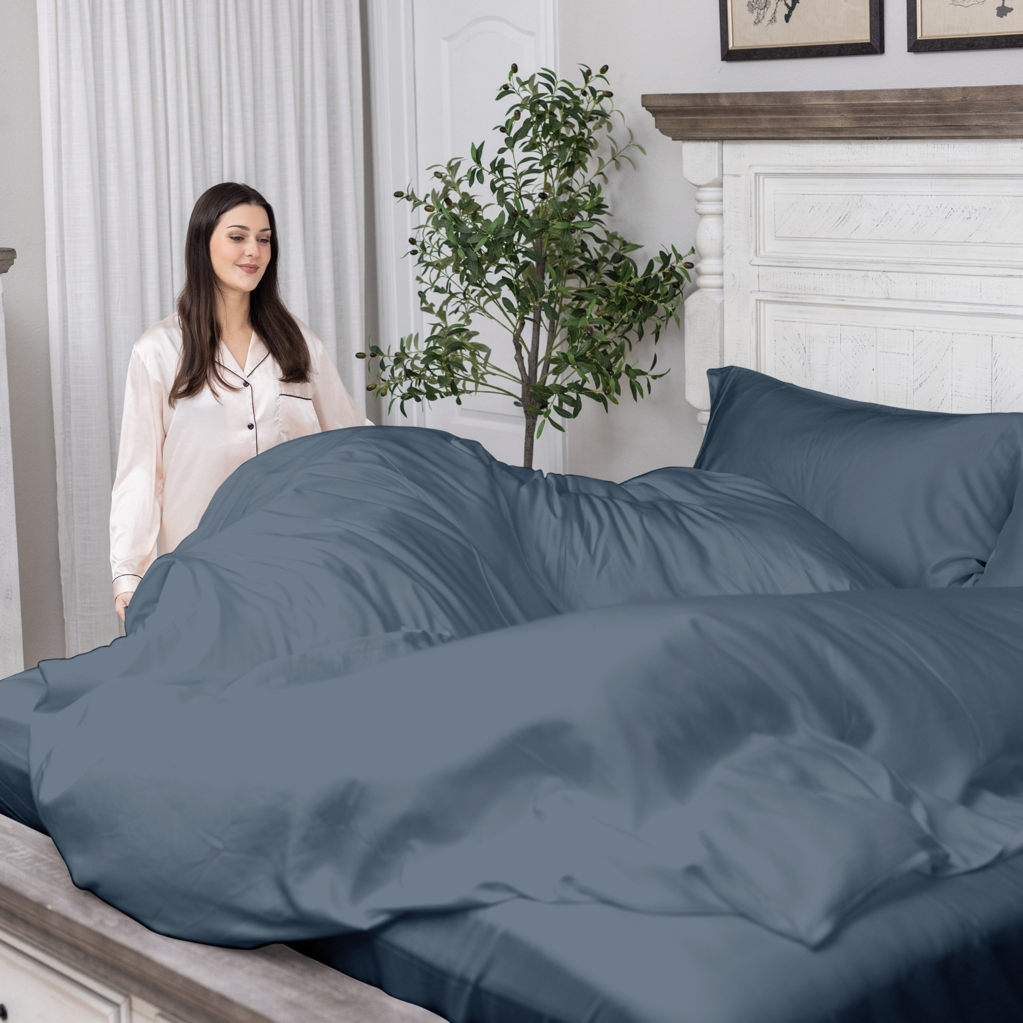 Woman standing next to a bed with blue bedding in a bedroom setting.