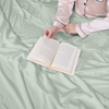 Person in pajamas holding an open book on a light green bedspread