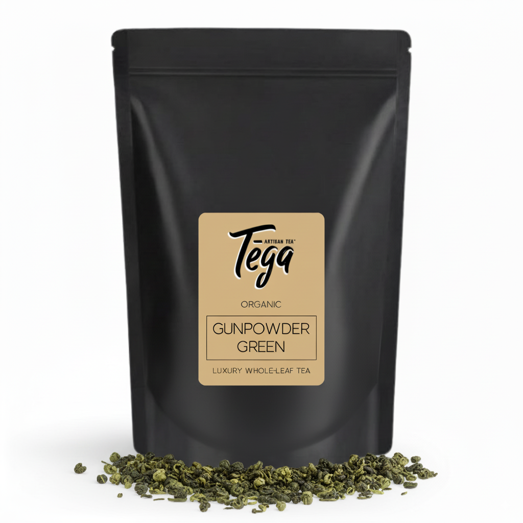 Black tea packaging with Tega label and loose tea leaves on a white background