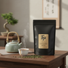Black tea package labeled 'Tega' on a wooden table with a teapot and cup in a serene setting.
