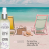 Glimmer Goddess organic silky dry body oil bottle on a beach with lounge chairs and a hat.