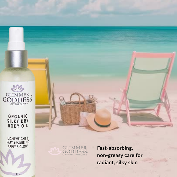 Glimmer Goddess organic silky dry body oil bottle on a beach with lounge chairs and a hat.