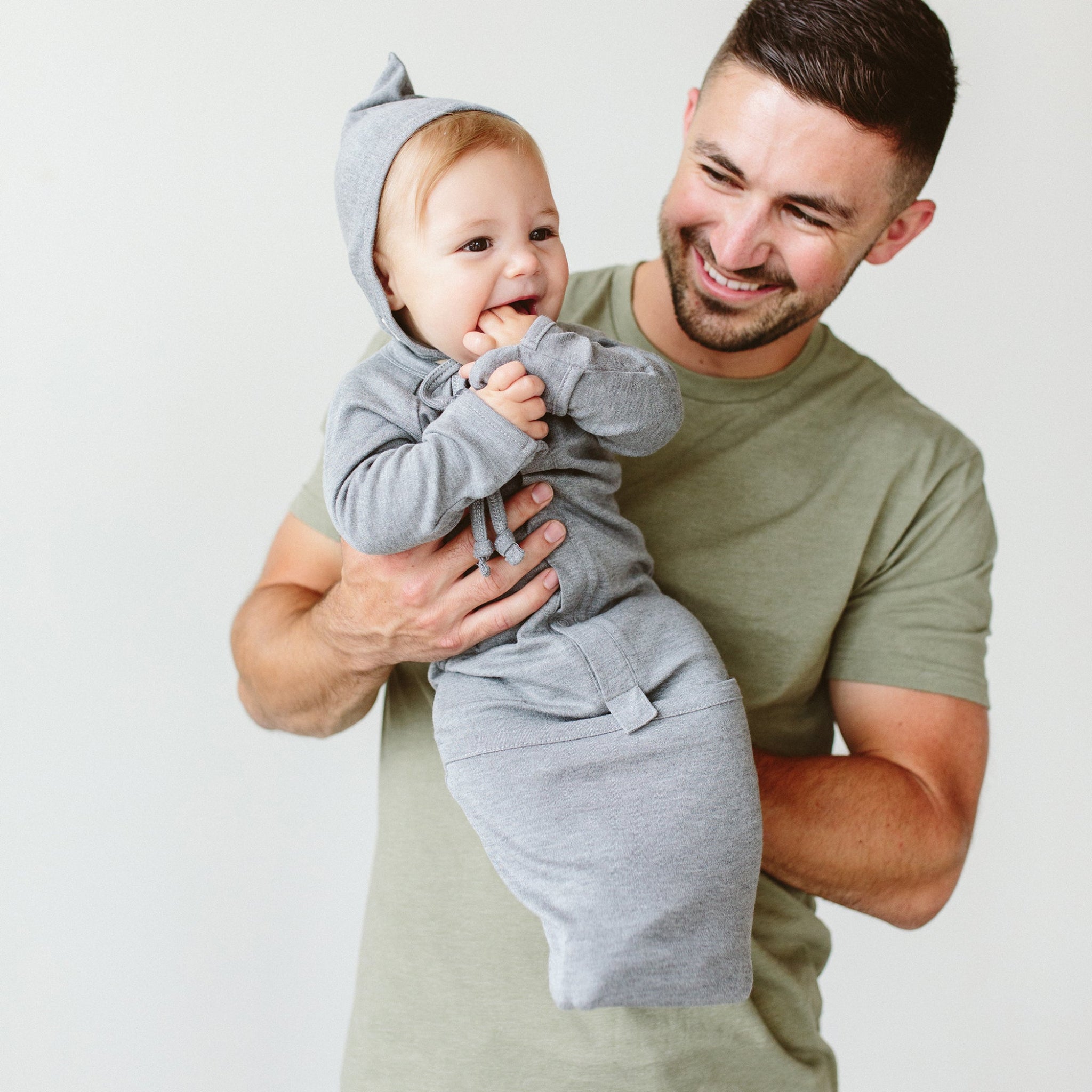 Man holding a baby wrapped in a gray swaddle against a plain background