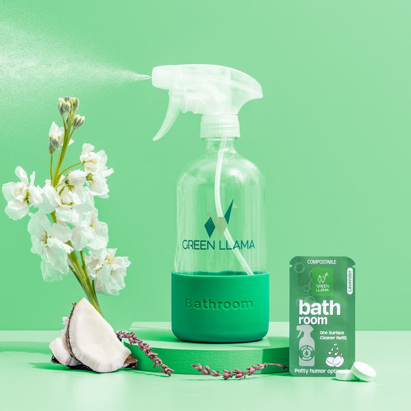 Green llama bathroom cleaning spray bottle with flowers and packaging on a green background. Green Llama Starter Home Cleaner Kit – 3-in-1 eco cleaning bundle with glass bottles & compostable refills. Plastic-free, non-toxic & naturally fragranced.