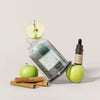 Jar of green tea, apple, cinnamon sticks, and bottle with dropper on a light background