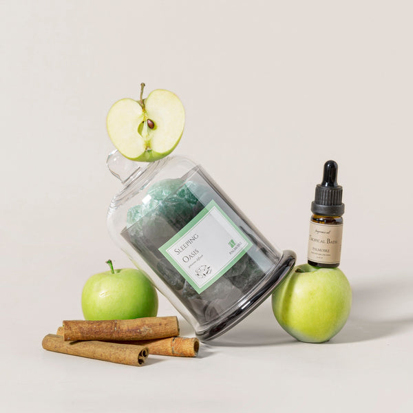 Jar of green tea, apple, cinnamon sticks, and bottle with dropper on a light background