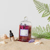Glass bottle with a purple label on a sandy surface with plants and shells.
